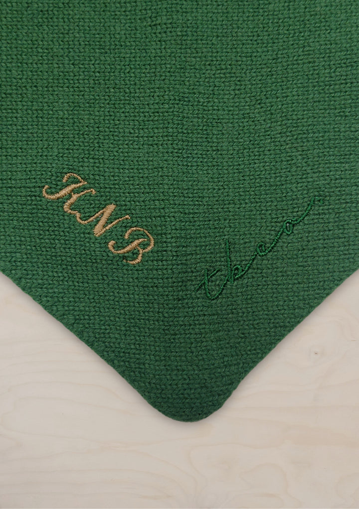 Close-up detail of TBCo Merino Triangle Scarf showing green knit texture with gold embroidered monogram and signature