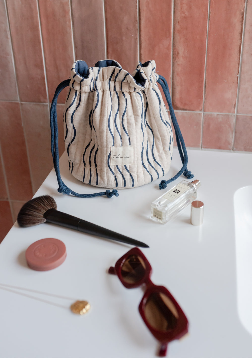 TBCo Cotton Wash Bag in Blue Wave pattern, cream fabric with navy stripes and drawstring closure, displayed with beauty accessories