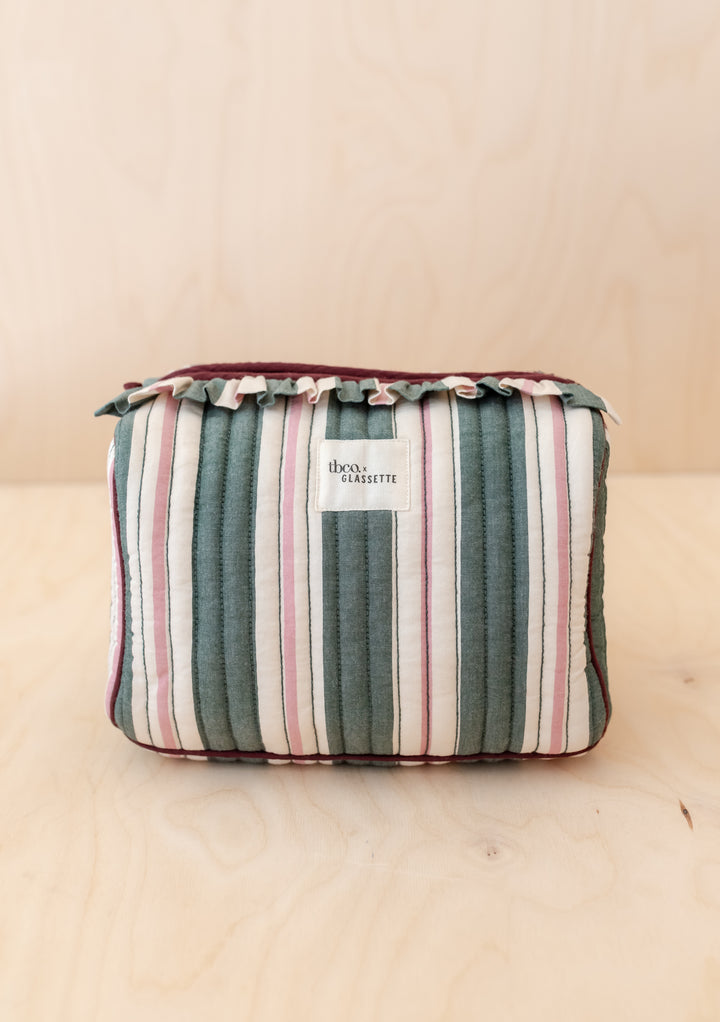 TBCo x Glassette Cotton Wash Bag in Green Stripe, featuring quilted fabric, vertical stripes, ruffled trim, and a front label on a wooden surface.