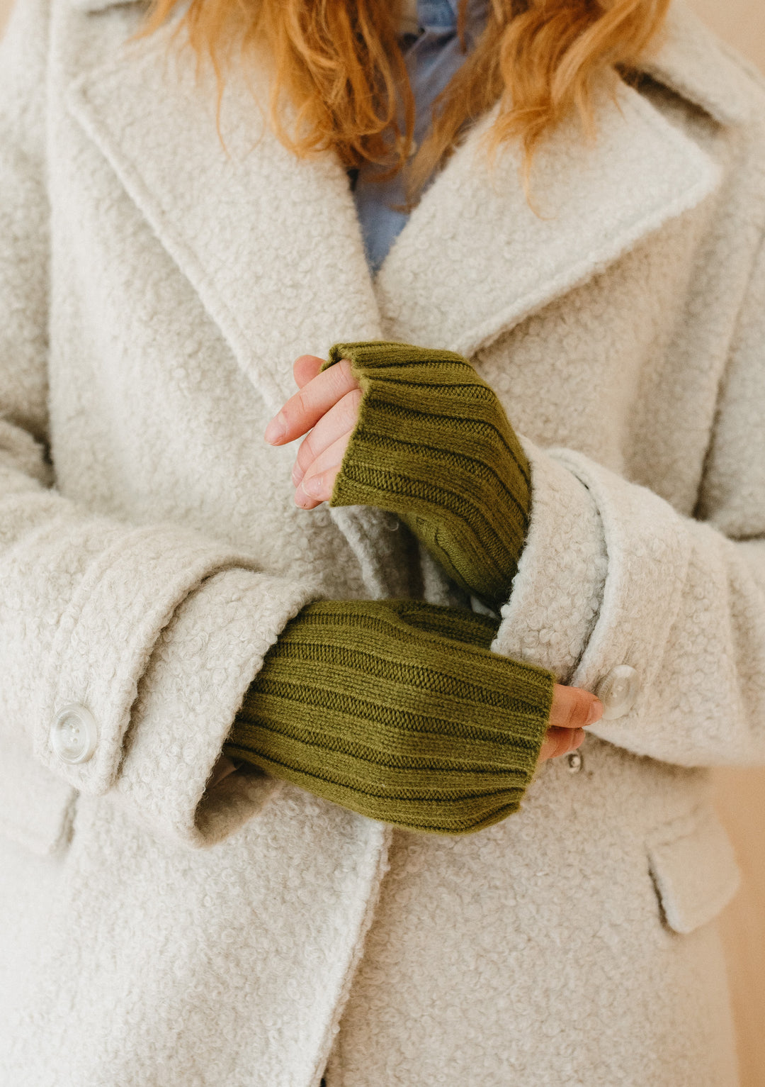 TBCo Cashmere & Merino Wrist Warmers in Olive shown on hands against cream winter coat, displaying ribbed knit texture