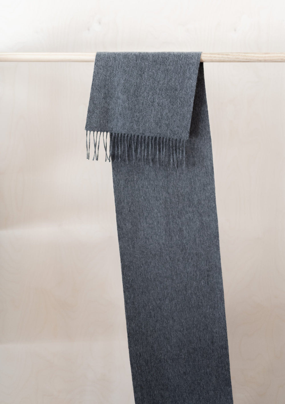 Luxurious TBCo pure cashmere scarf in charcoal melange with fringed ends, elegantly draped over wooden rail