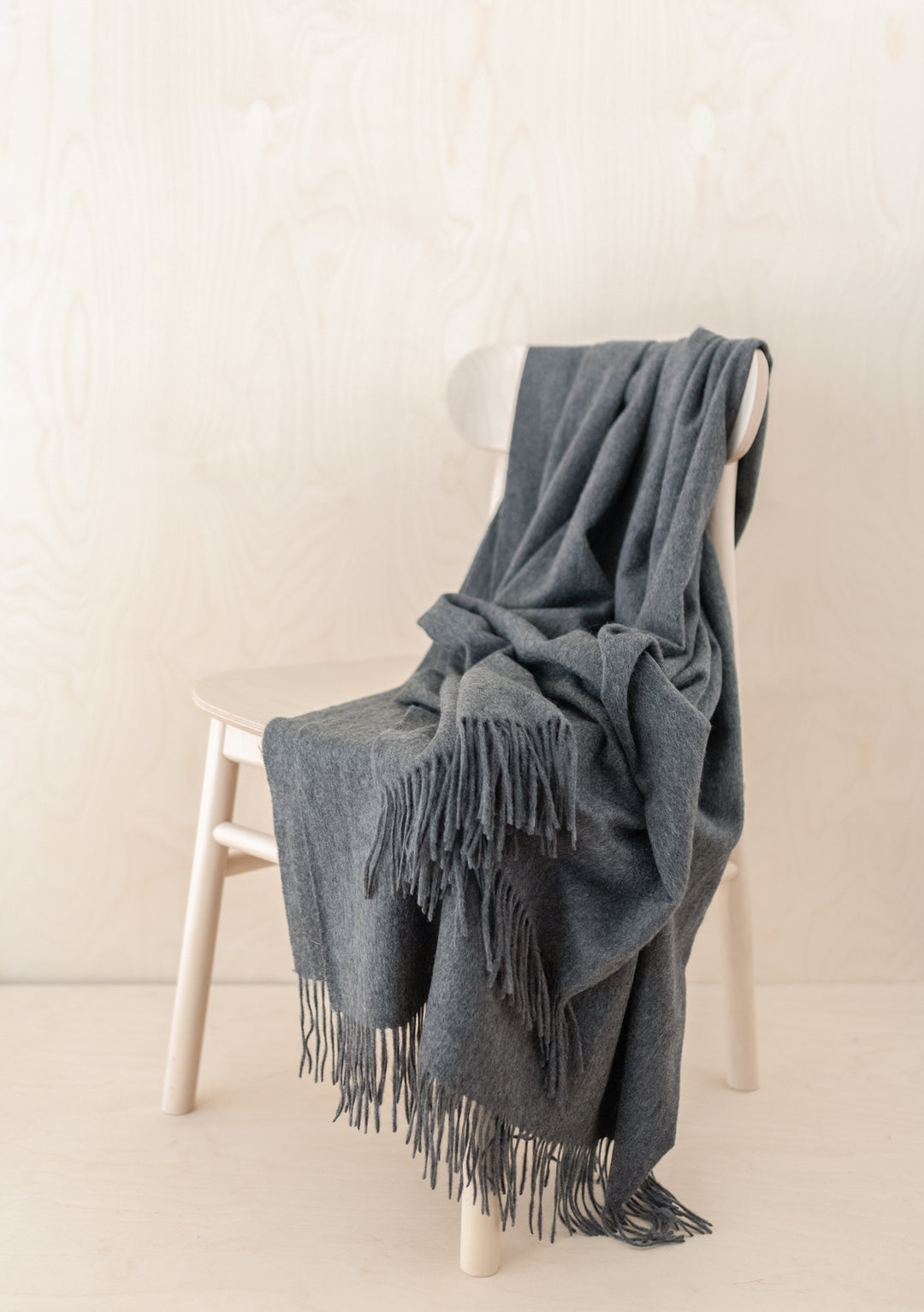 TBCo Cashmere Small Blanket in Charcoal Melange draped elegantly over white chair, showcasing soft texture and fringed edges