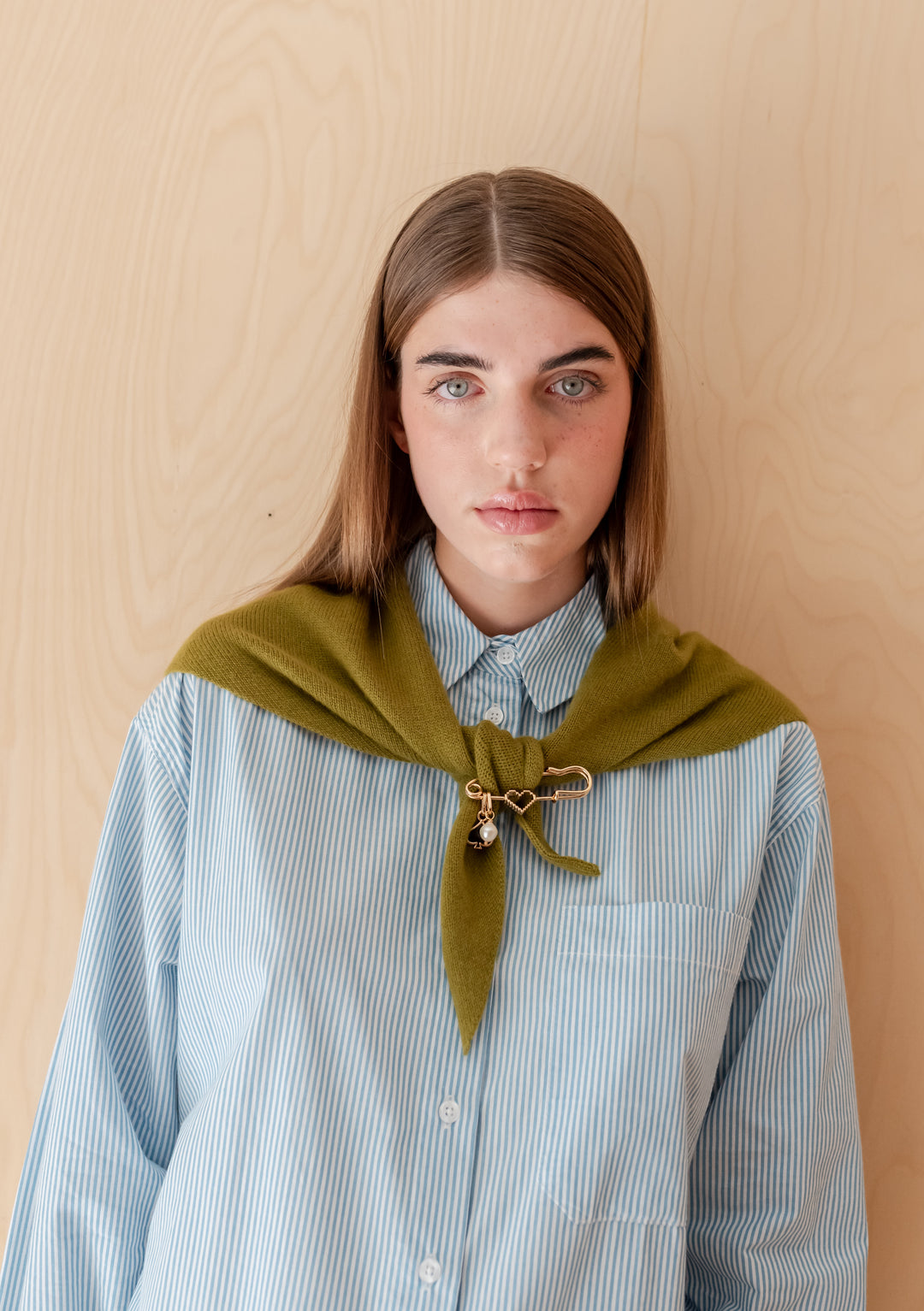 Young woman wears TBCo x frkl. Circus Scarf Pin on olive merino wool triangle scarf, featuring gold-tone safety pin design with charms, complementing her minimalist outfit.
