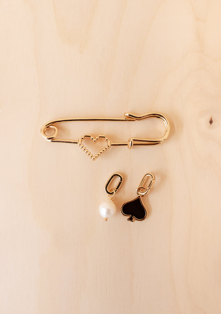 TBCo x frkl. Circus Scarf Pin: A gold-tone safety pin brooch with a pixelated heart and two charms—a pearl drop and a black spade.
