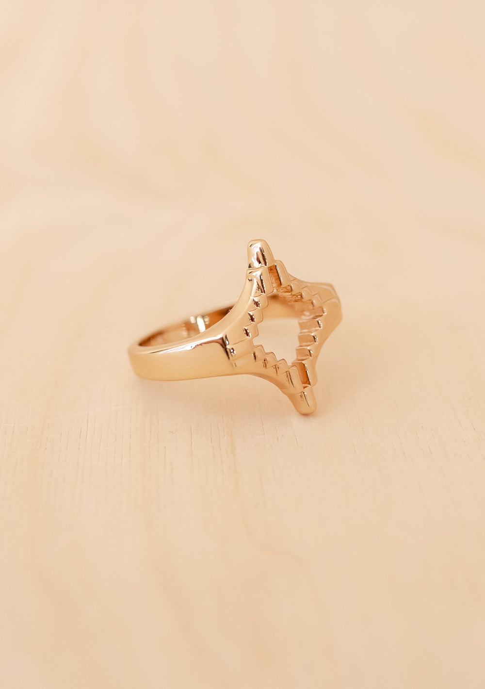 TBCo x frkl. Diamond Scarf Ring featuring a star-like, pixelated design in gold-toned brass, resting on a light wooden surface. Ideal for securing wool triangle scarves.