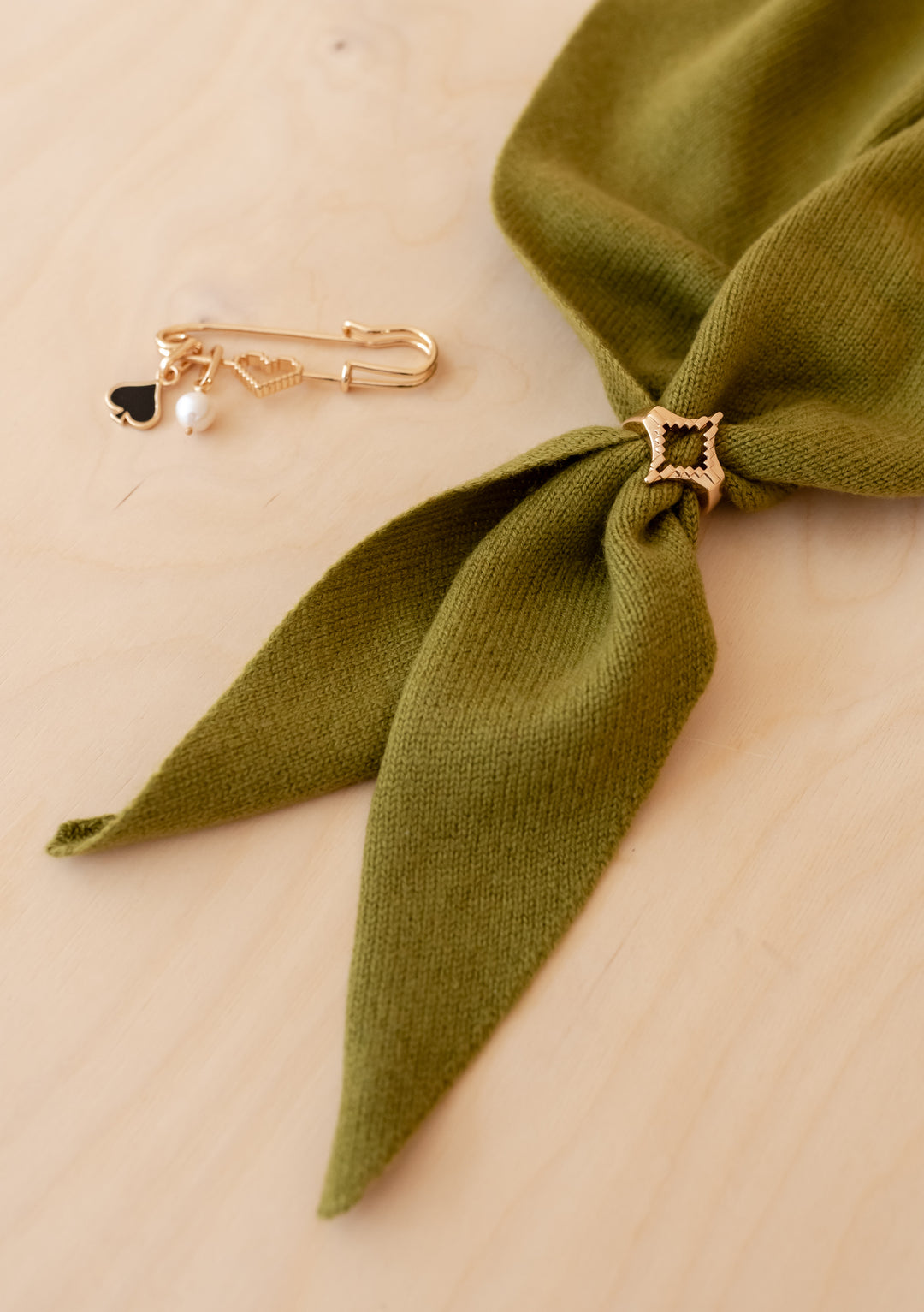 TBCo x frkl. Diamond Scarf Ring: Olive-green knitted merino wool triangle scarf threaded through star-shaped gold-tone ring and paired with a matching brooch featuring charms.